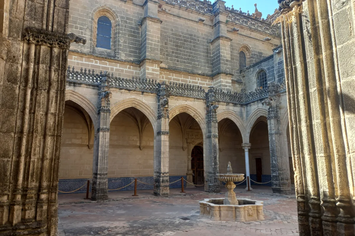 A small Gothic cloister with pointed arches and a stone fountain in its courtyard, seen between two carved columns
